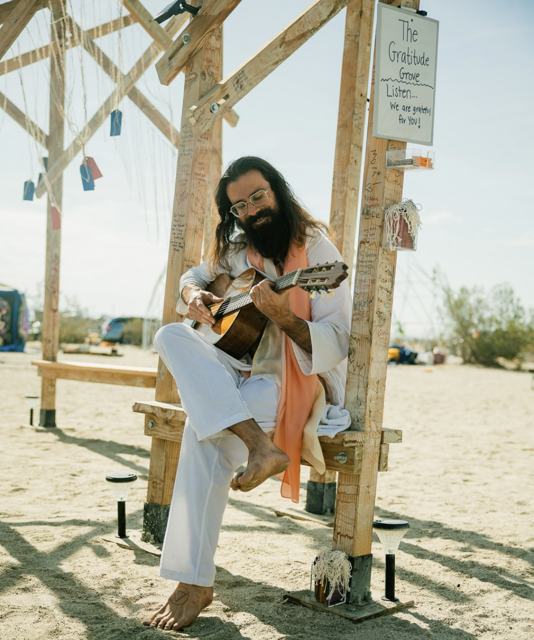 Awe playing guitar beneath the wooden arch of the Gratitude Grove